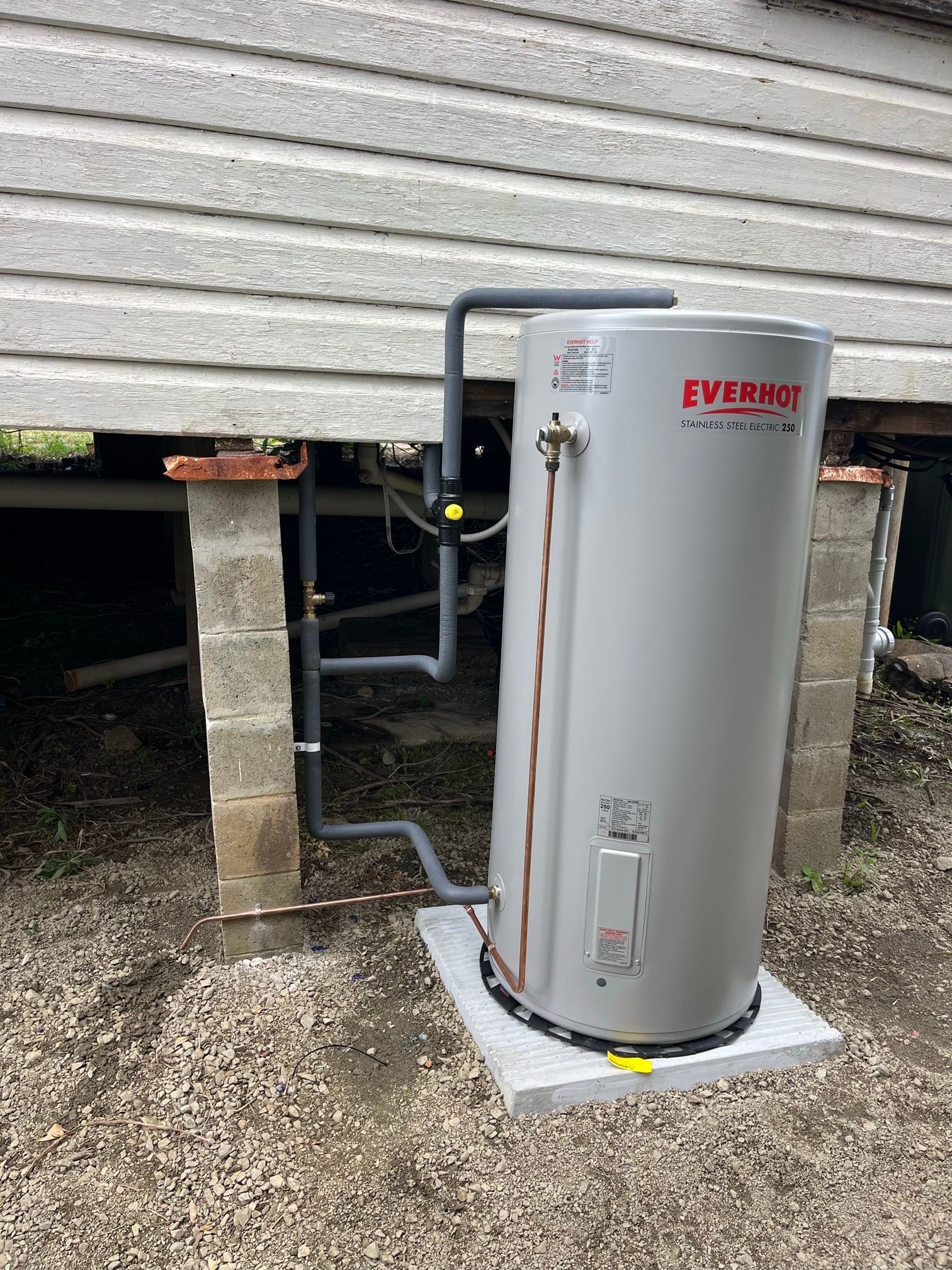 A vertical Everhot water heater outside a building, pipes connected, set on a concrete pad. — VR Marsden Plumbing in Red Rock, NSW