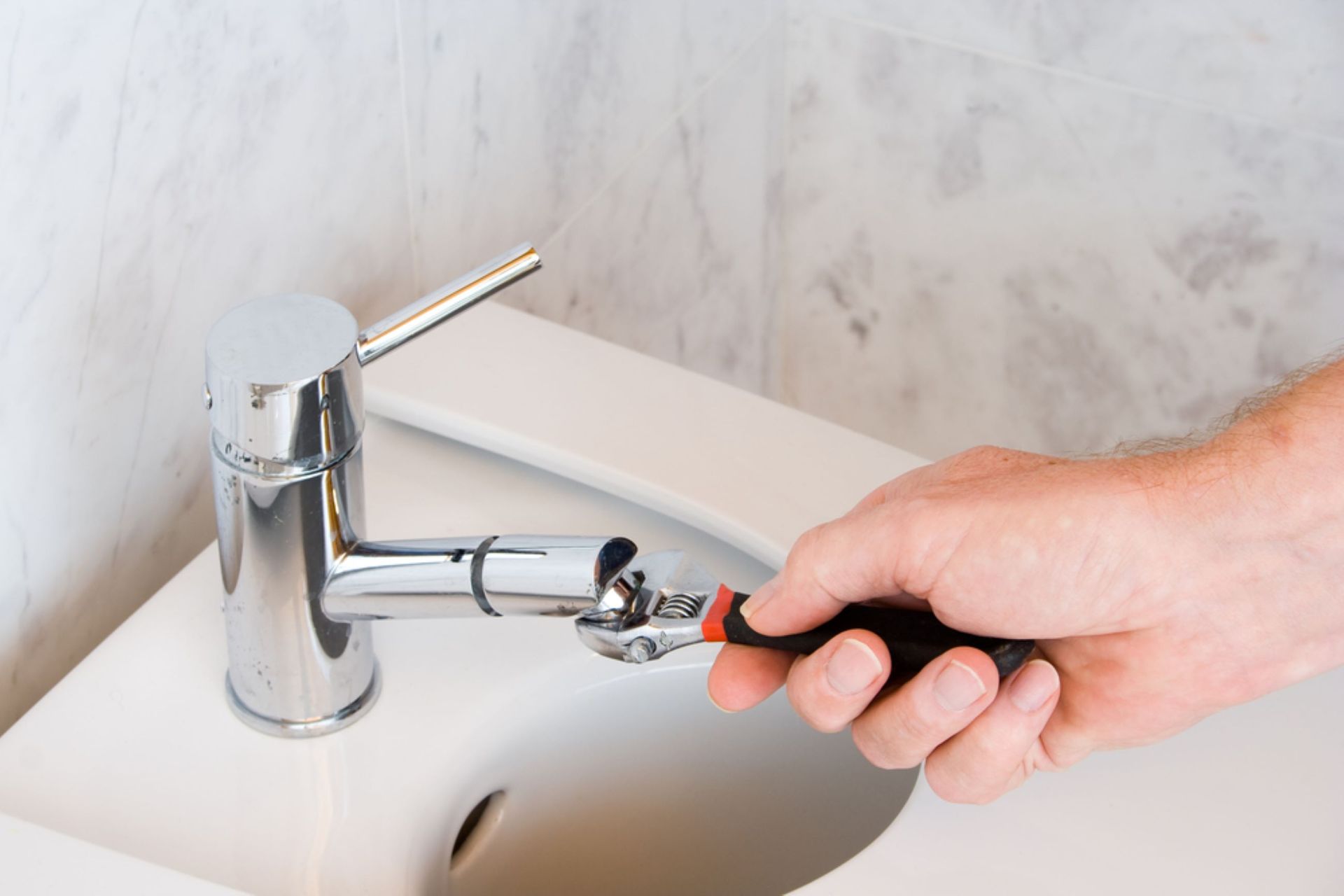 A Hand Tightening a Faucet With a Wrench in a White Sink — VR Marsden Plumbing in Red Rock, NSW