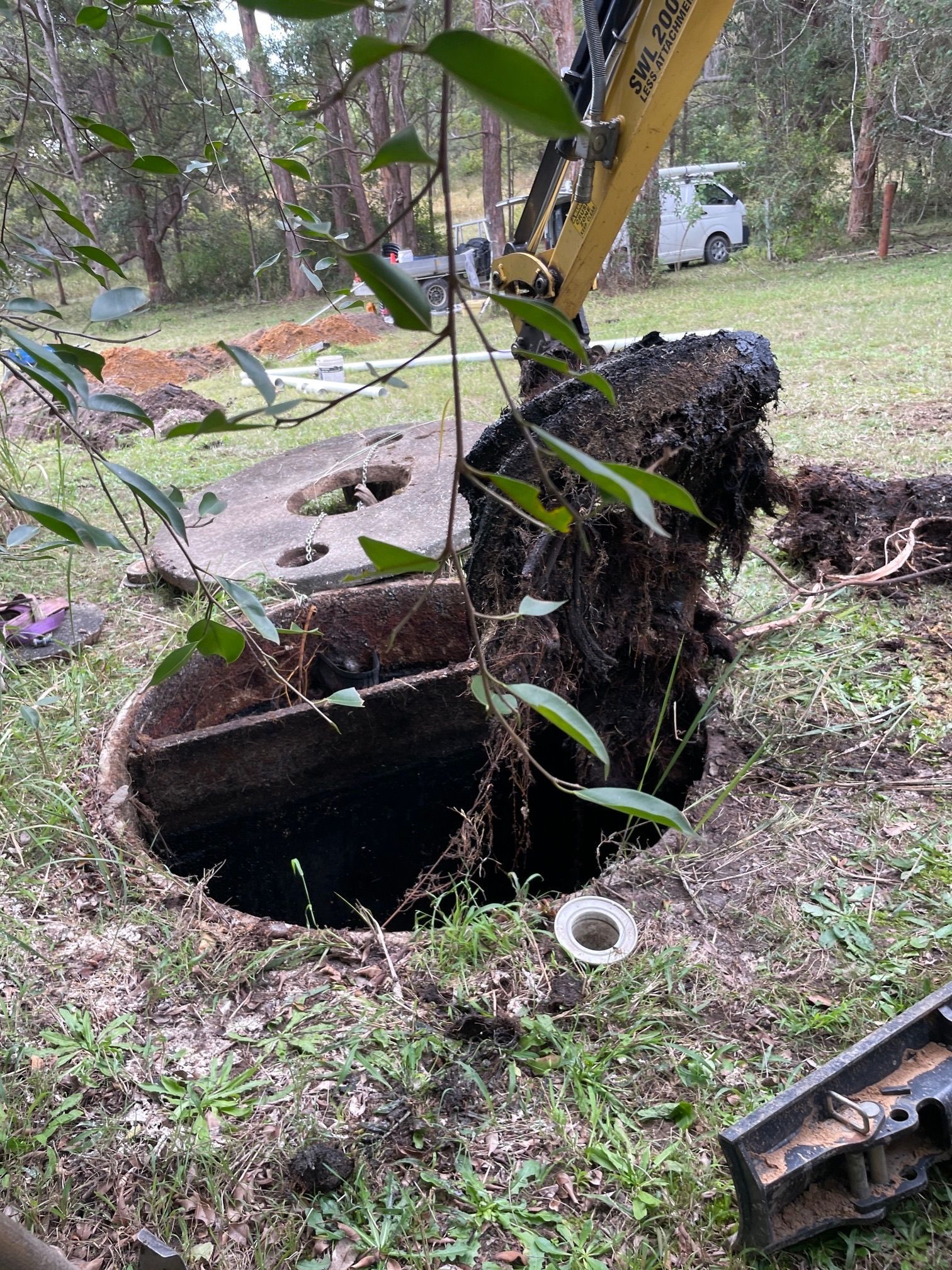 Excavator lifts an open septic tank lid in a grassy yard— VR Marsden Plumbing in Red Rock, NSW