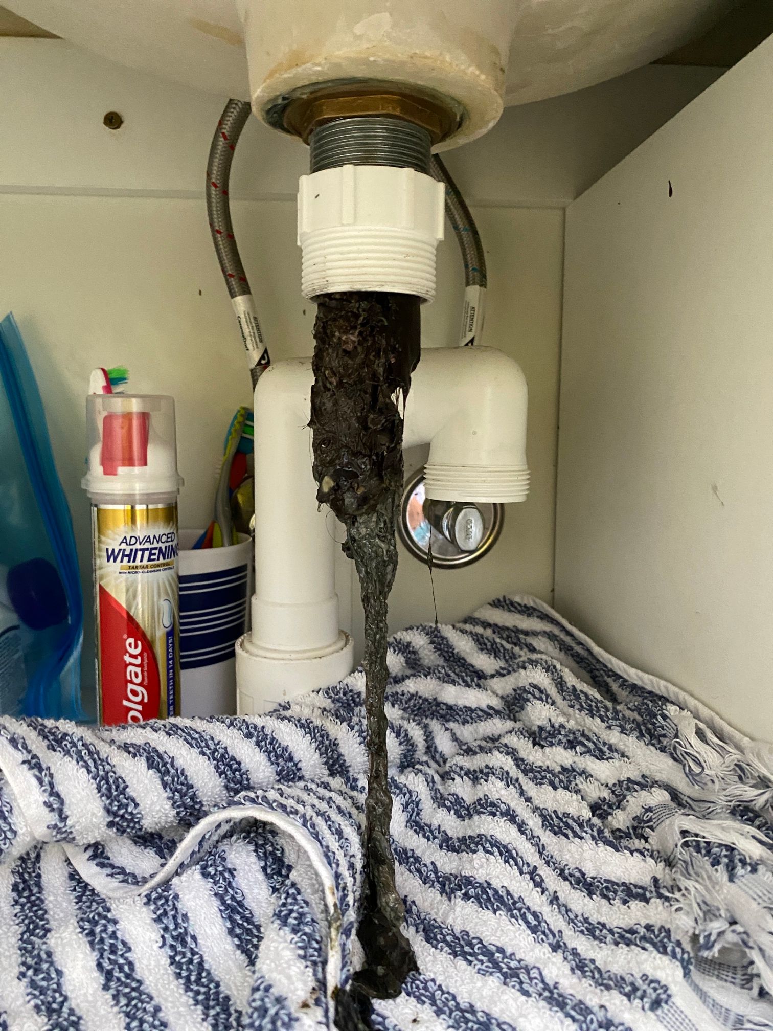 A clogged sink drain with a long, dark mass of debris hanging below the pipe. A towel and toiletries are nearby— VR Marsden Plumbing in Red Rock, NSW