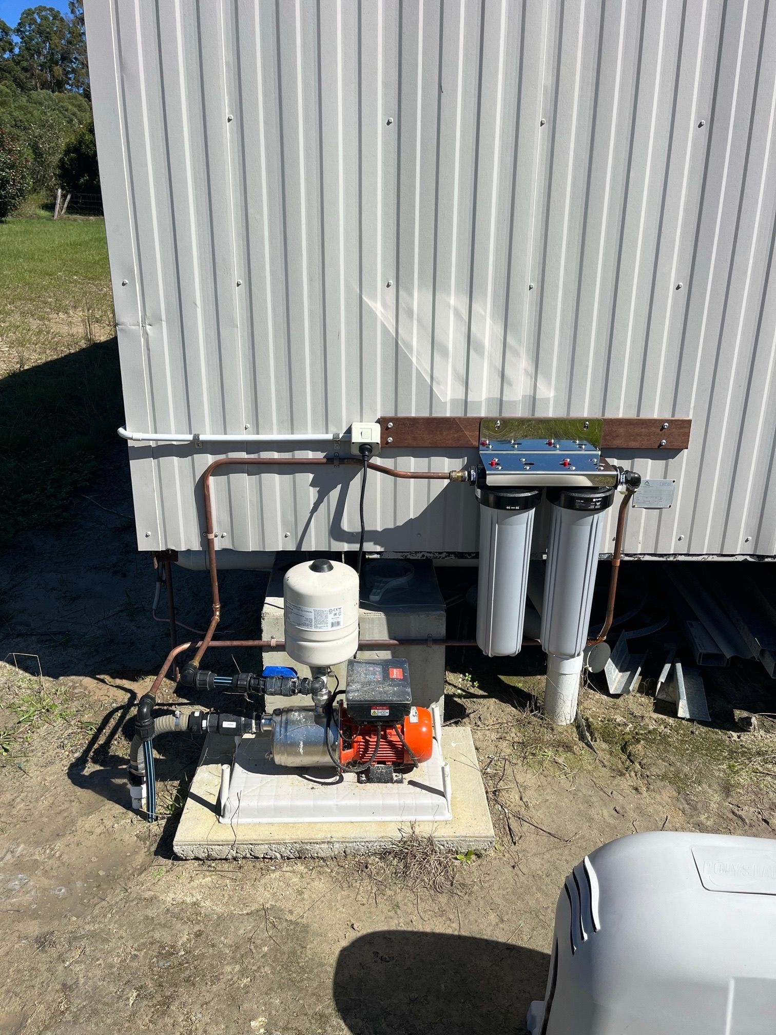 Water pump and filtration system on concrete pad, installed on building's exterior. Copper pipes visible— VR Marsden Plumbing in Red Rock, NSW