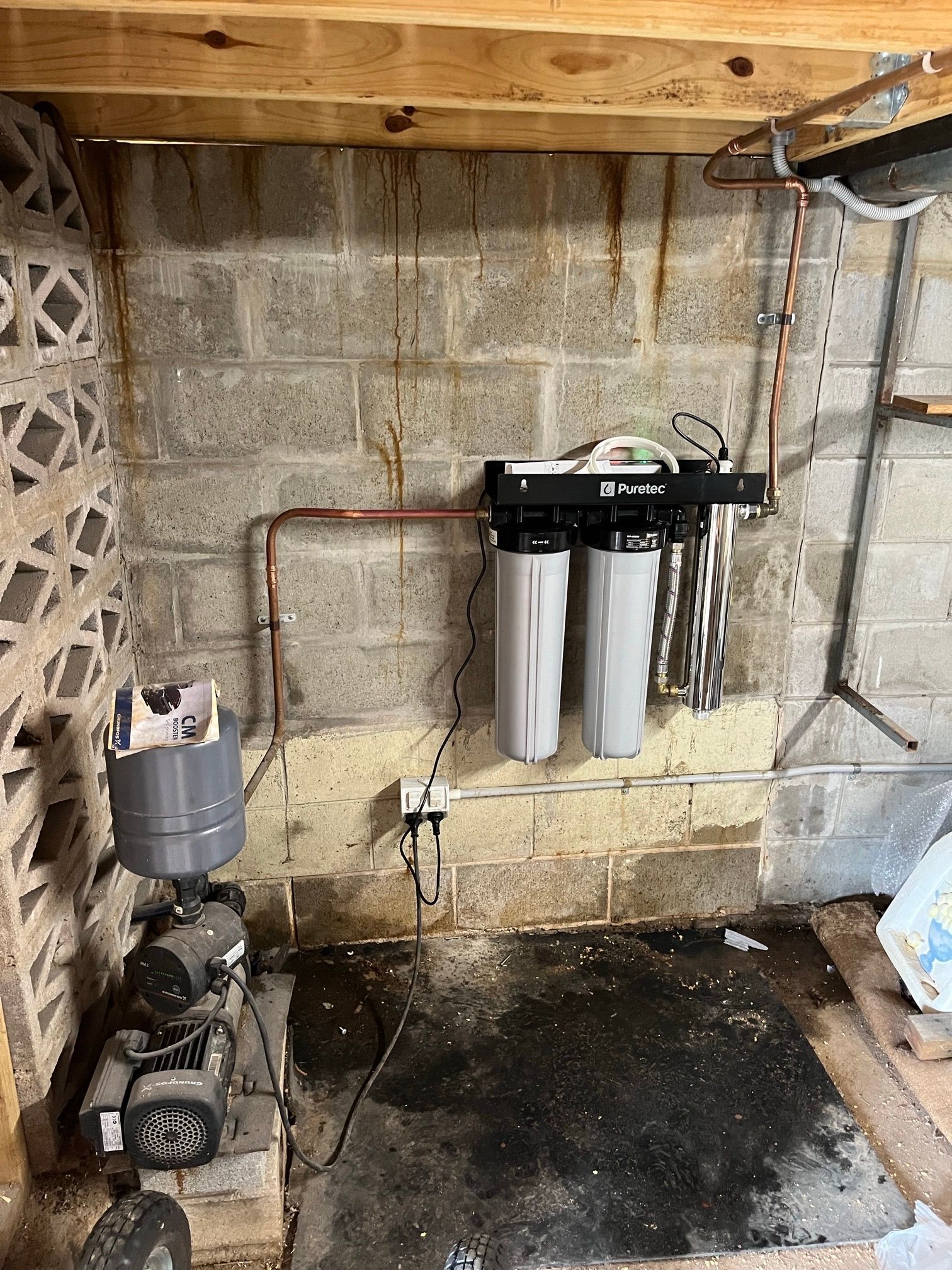 Water filtration system mounted on a cinder block wall in a basement. Copper pipes, filters, and a water pump visible— VR Marsden Plumbing in Red Rock, NSW