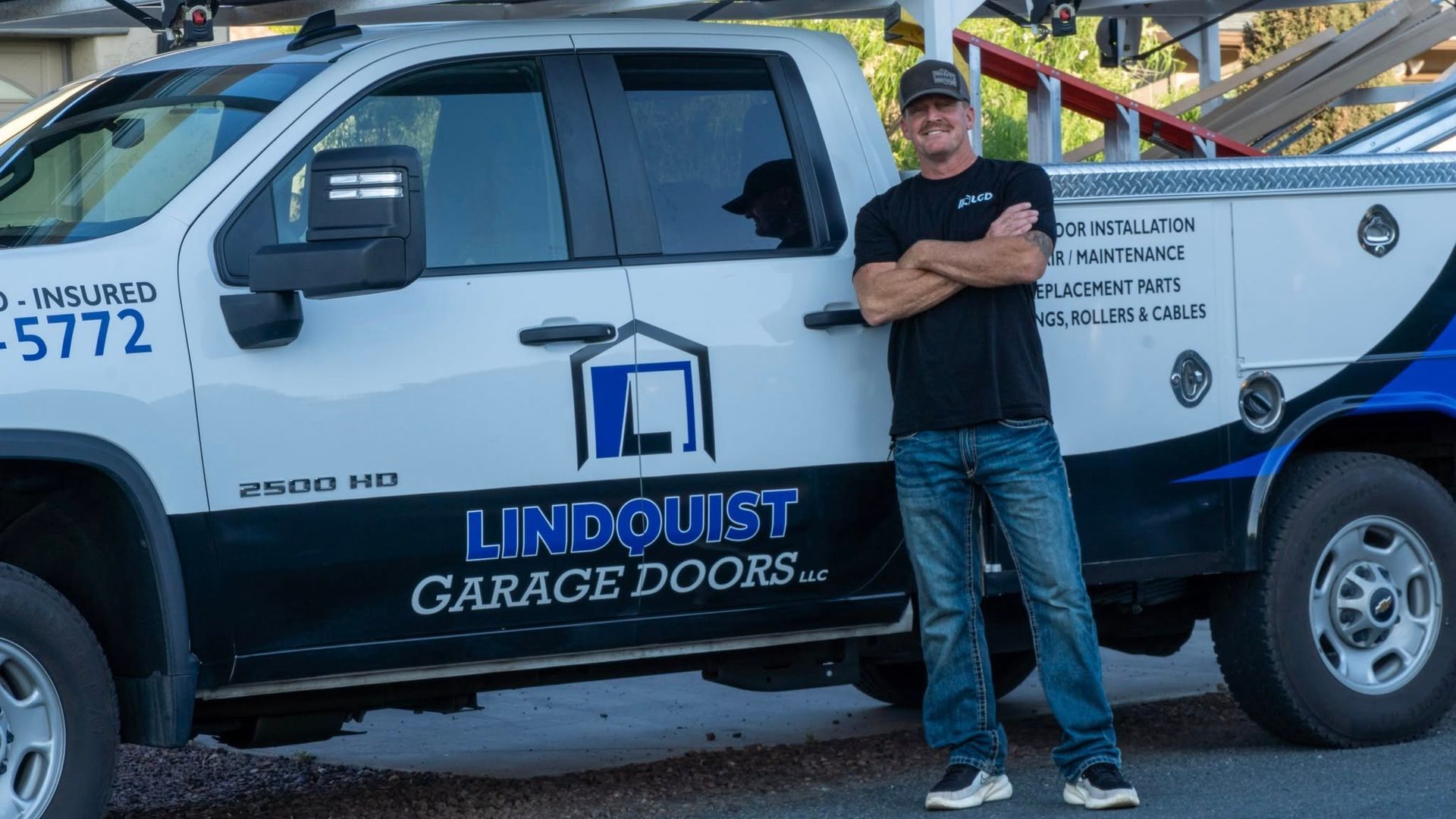 Man standing in front of a truck with his company logo, Lindquist Garage Doors. The man is smiling with arms crossed.