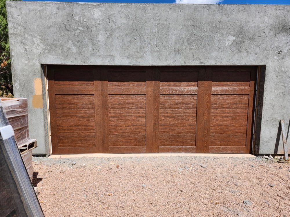 Brown garage door with four panels set in a concrete frame, on a gravel driveway.