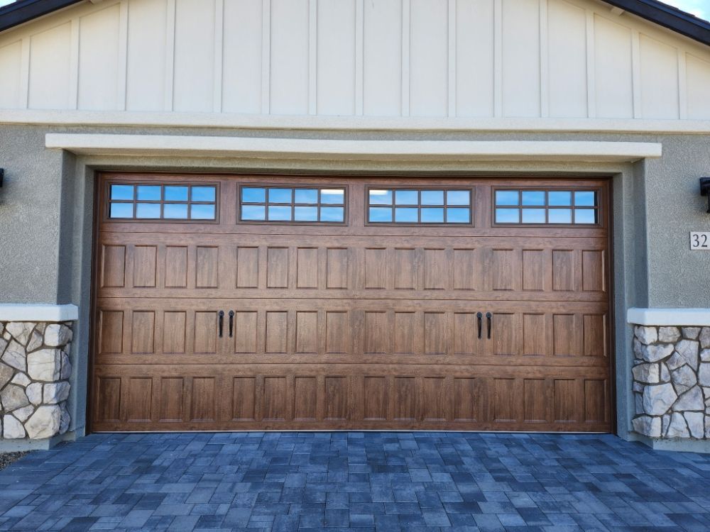 Brown garage door with windows above, set in a stone-accented frame, on a brick-paved driveway.