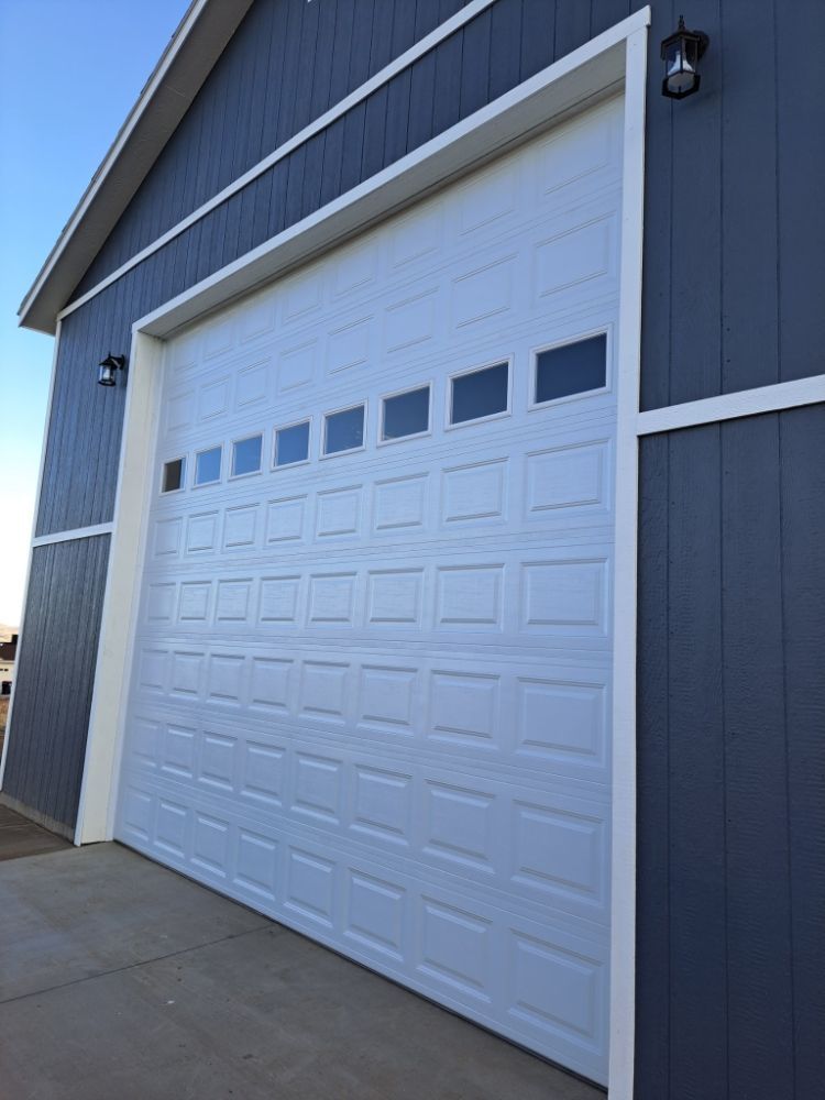 White garage door on a blue building. The door has windows across the top and two lights above it.