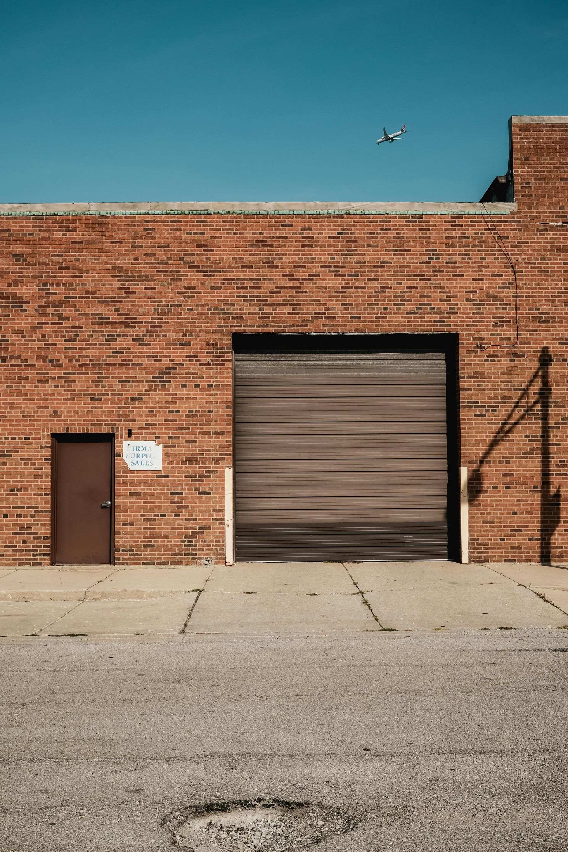 Brick building with a closed garage door and a small door, both brown. A plane flies overhead.