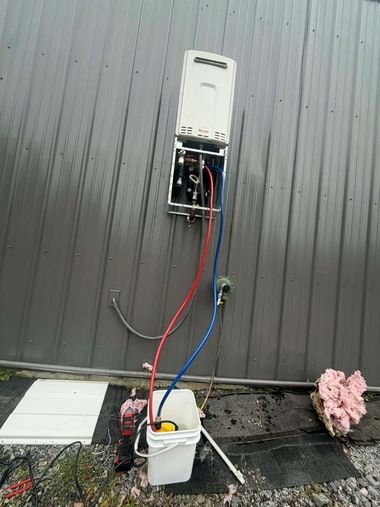 A wall-mounted tankless water heater with exposed pipes connected to a bucket with a pump for maintenance or flushing.