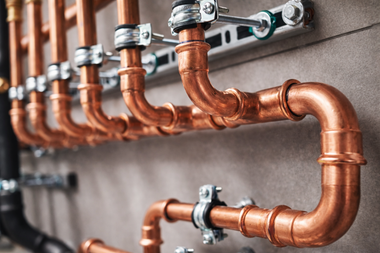 Close-up of a network of interconnected shiny copper pipes mounted on a wall with metal pipe clamps.