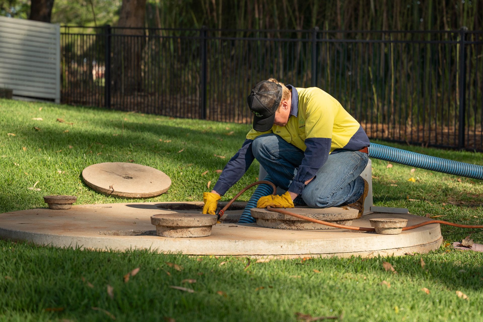 Worker Kneeling at an Open Manhole Cover on Grass — Shreks Septic Services in Gowrie Junction, QLD