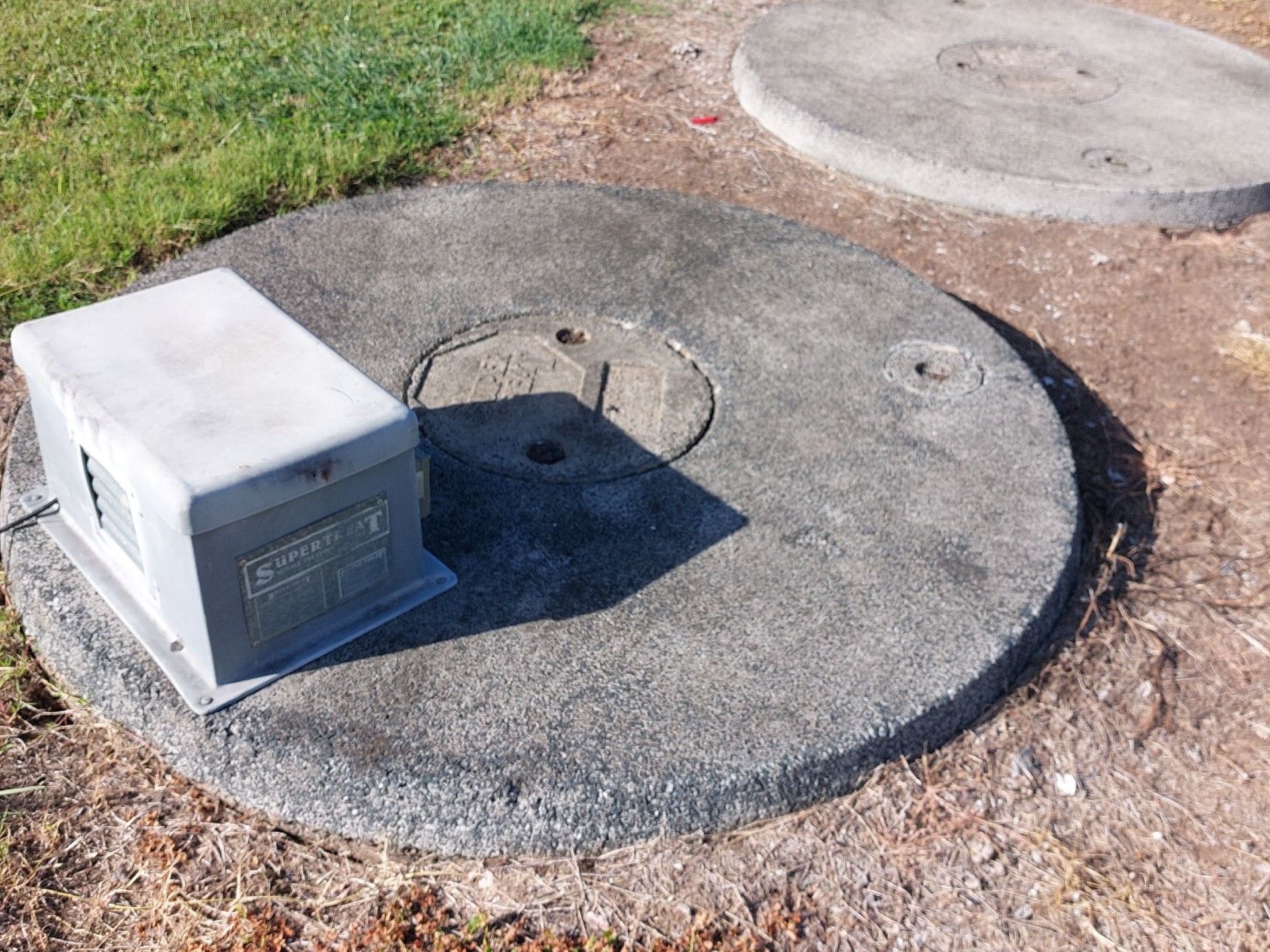 A Round Manhole Cover Near Grass — Shreks Septic Services in Gowrie Junction, QLD