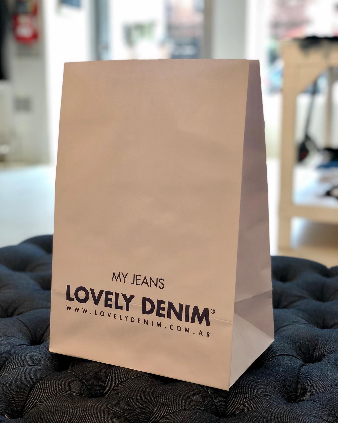 Una bolsa de papel blanca hecha de mezclilla hermosa reposa sobre una otomana negra.