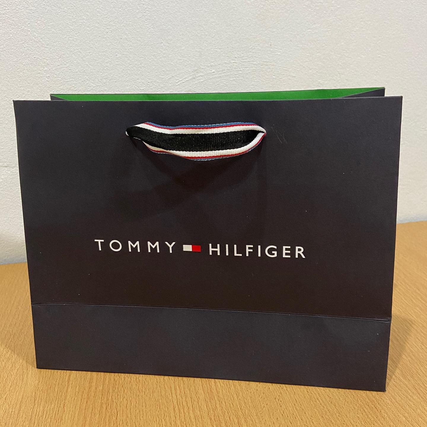 Un bolso Tommy Hilfiger negro está sobre una mesa de madera.