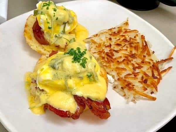 A White Plate Topped with Eggs Benedict and Hash Browns — Zen Luxury Retreats in Darwin City, NT