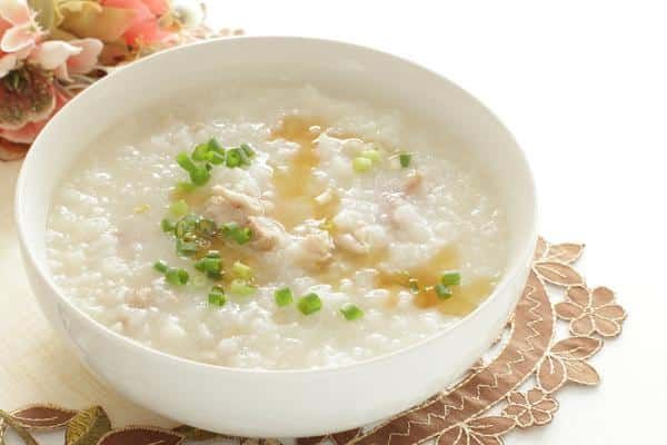 A Bowl of Porridge with Chicken and Green Onions on A Table — Zen Luxury Retreats in Darwin City, NT