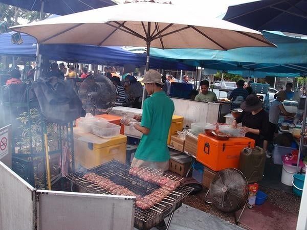 A Man in A Green Shirt Is Cooking Food on A Grill — Zen Luxury Retreats in Darwin City, NT