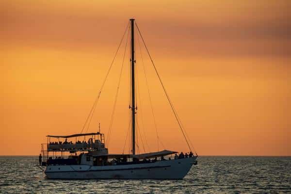 A Sailboat is Floating on Top of a Body of Water at Sunset — Zen Luxury Retreats in Darwin City, NT