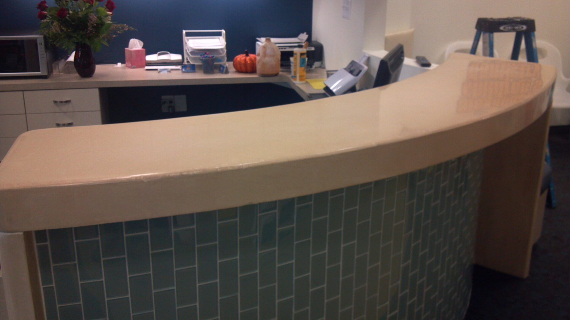 A curved polished concrete counter in a kitchen with blue tiles