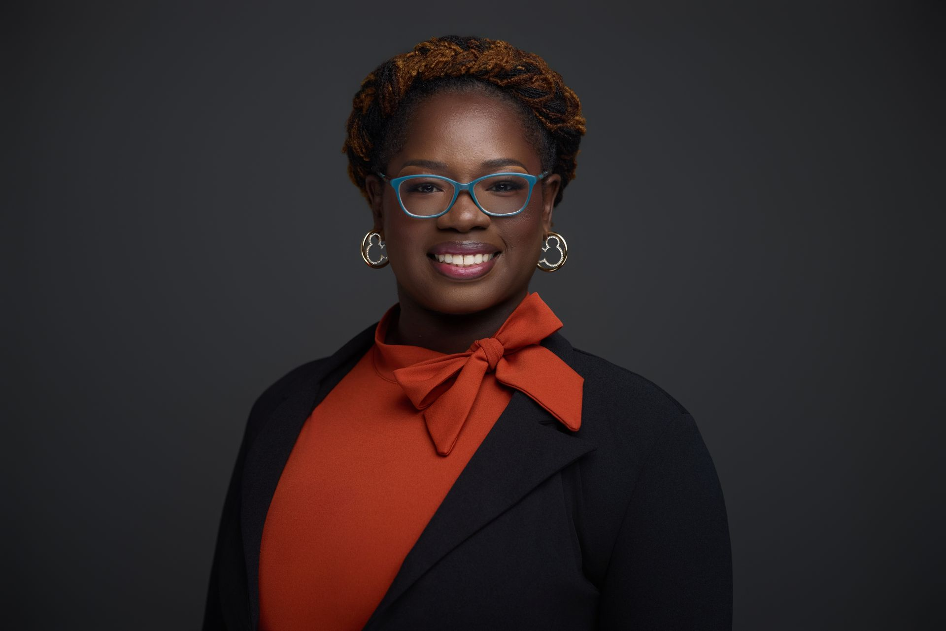 Woman with glasses and a red bow tie, smiling, wearing a black blazer.