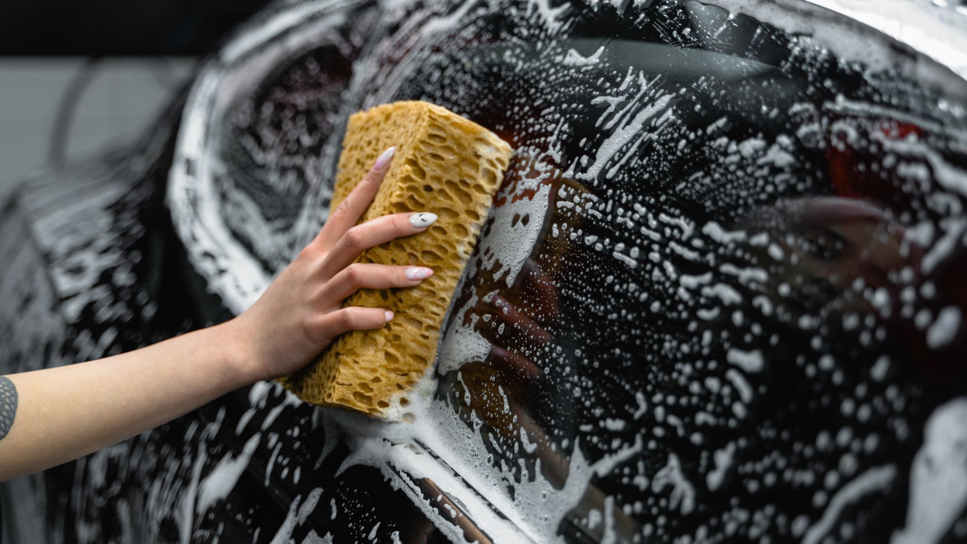 A woman is washing a car with a sponge.