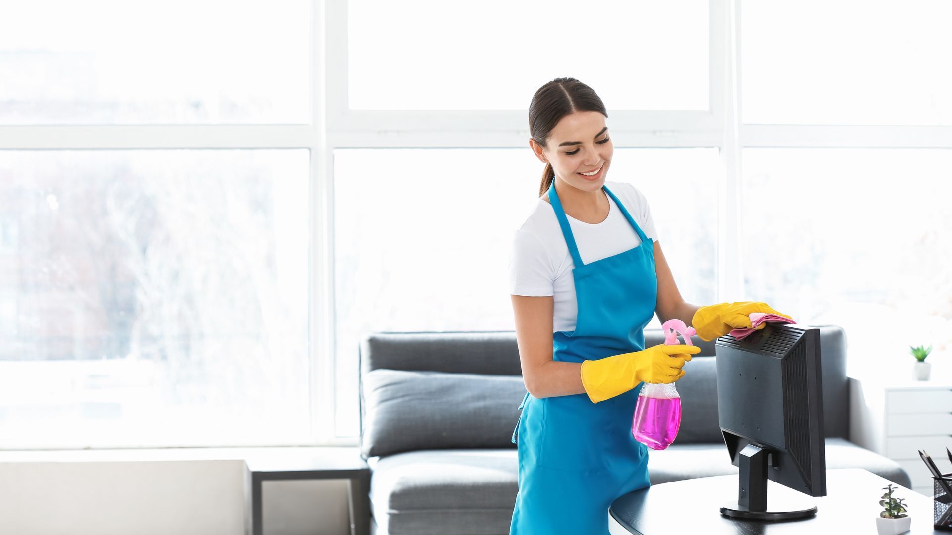 A woman is cleaning a computer monitor in a living room.