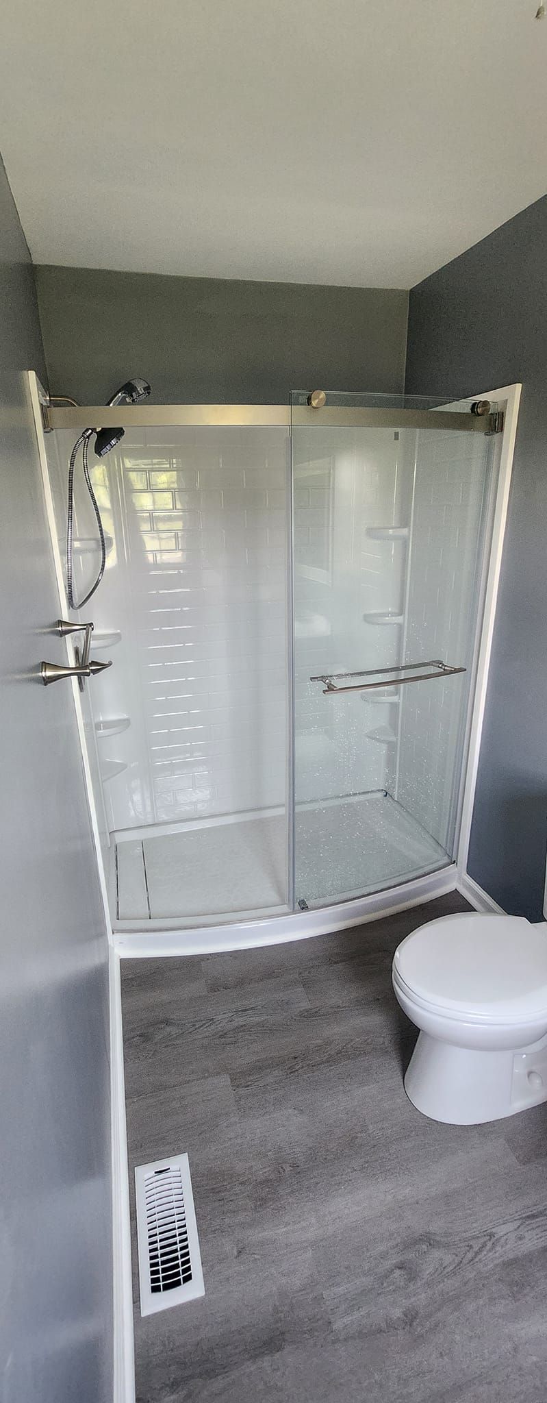 A bathroom with a gray floor and walls. A shower stall is in the center with a toilet to the right.