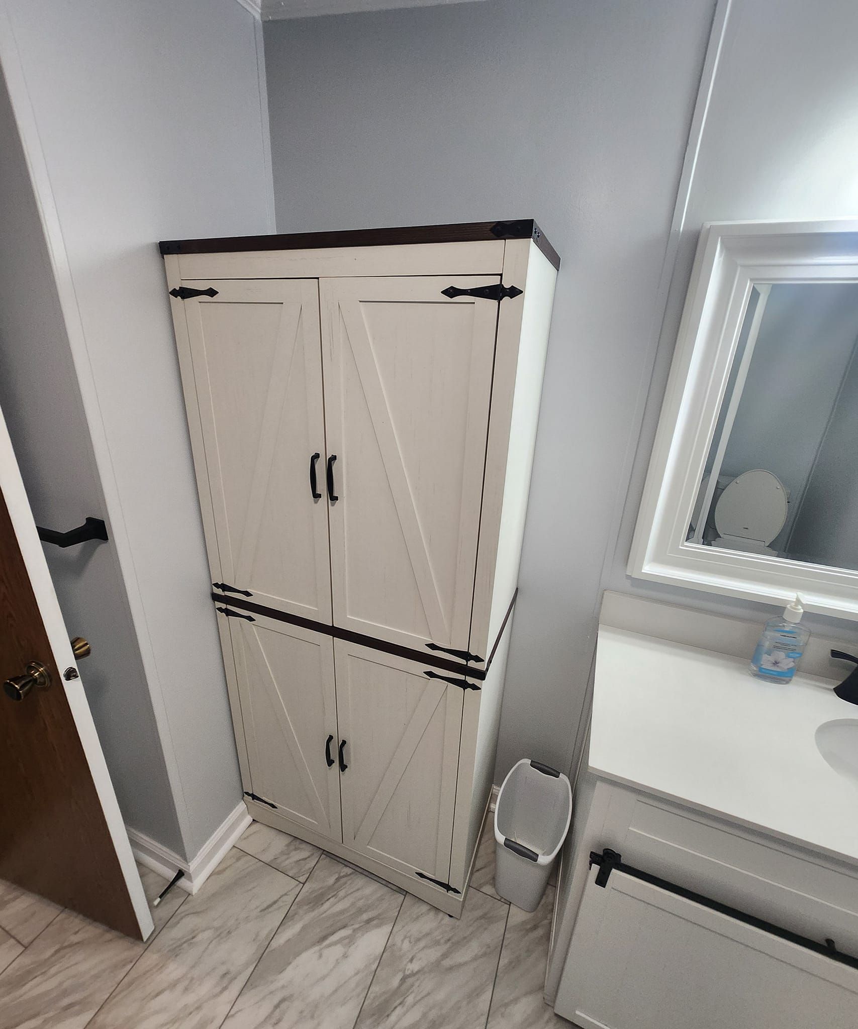 Tall white cabinet with black accents in a bathroom next to a sink with a mirror.