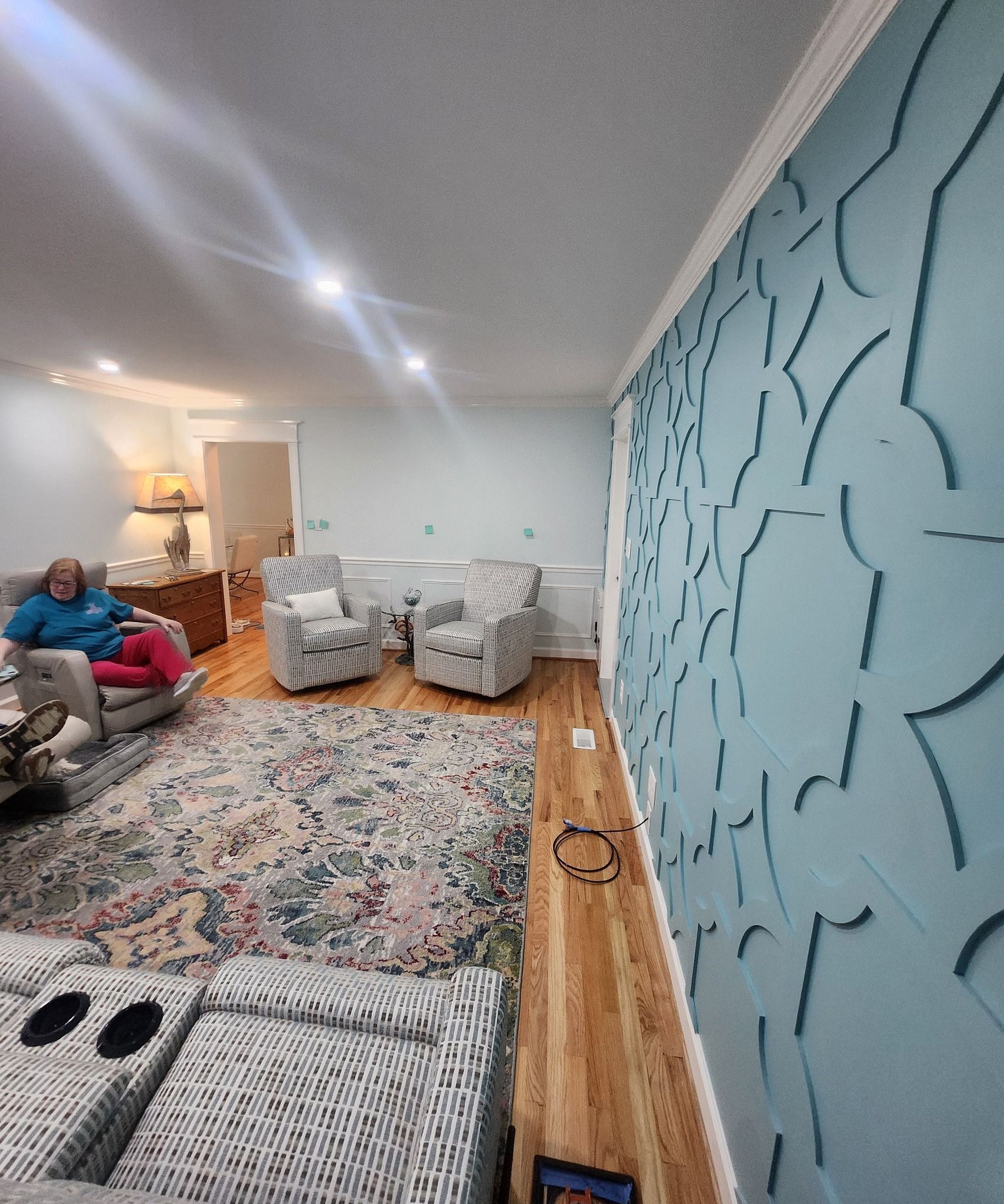 Living room with blue accent wall, patterned rug, armchairs, and seated person.