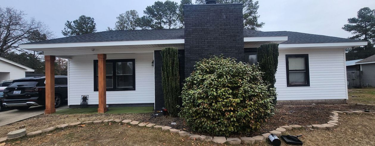 White house with black trim, a dark chimney, and brown columns on a cloudy day.