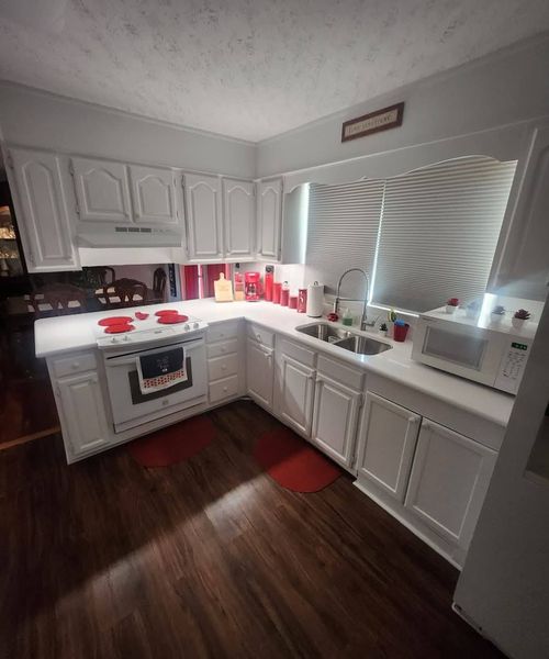 White kitchen with cabinets, stove, sink, and microwave; red accents and dark wood floors.