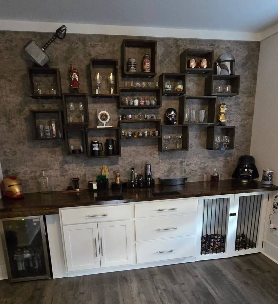 Bar with a wall display of boxes, various glasses and decor on a textured wall.  White cabinets below.