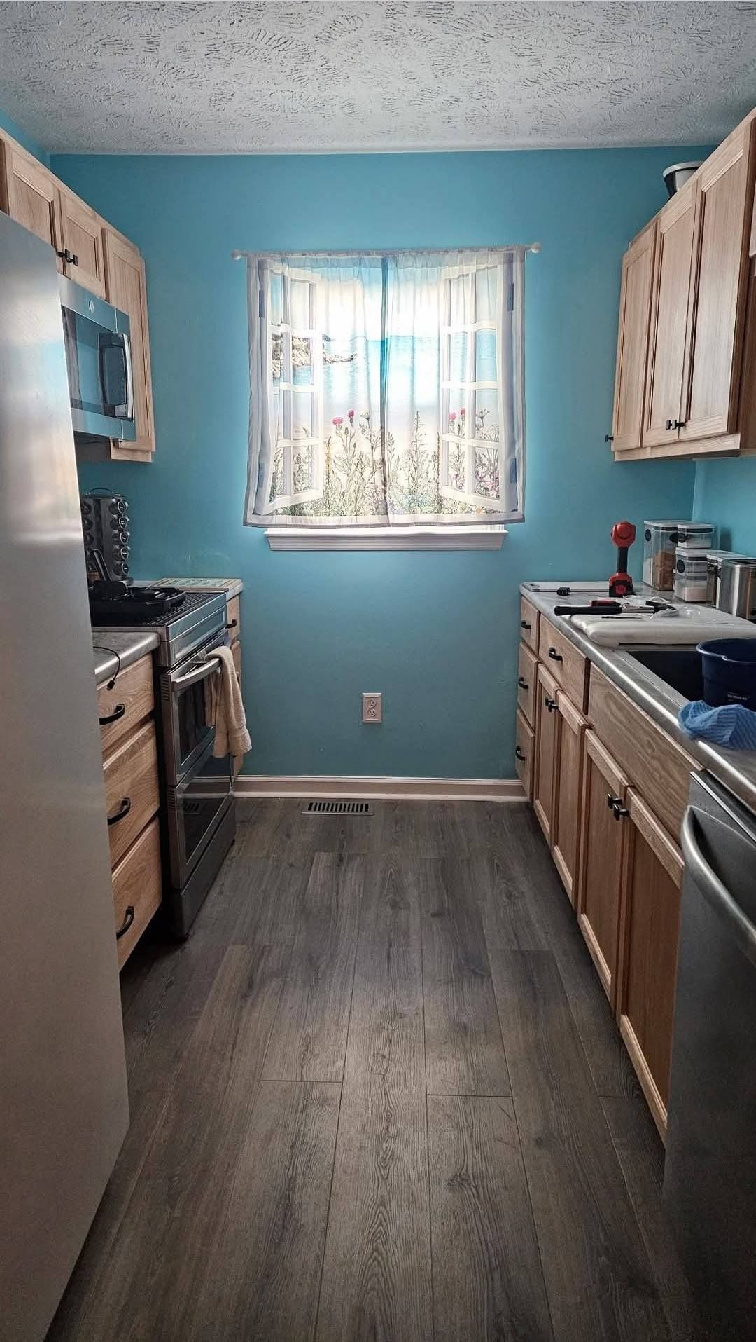 Kitchen with light wood cabinets, gray floor, blue walls, and window with sunlight.