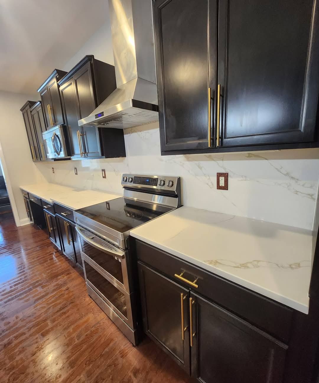 Modern kitchen with dark cabinets, stainless steel appliances, and white countertops.
