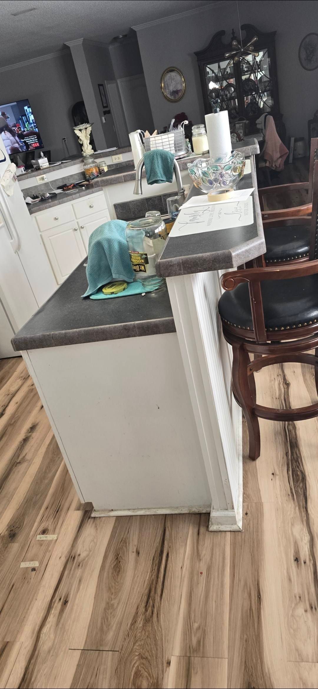 Kitchen island with white cabinets, dark countertop, and wood floors. A barstool sits nearby.