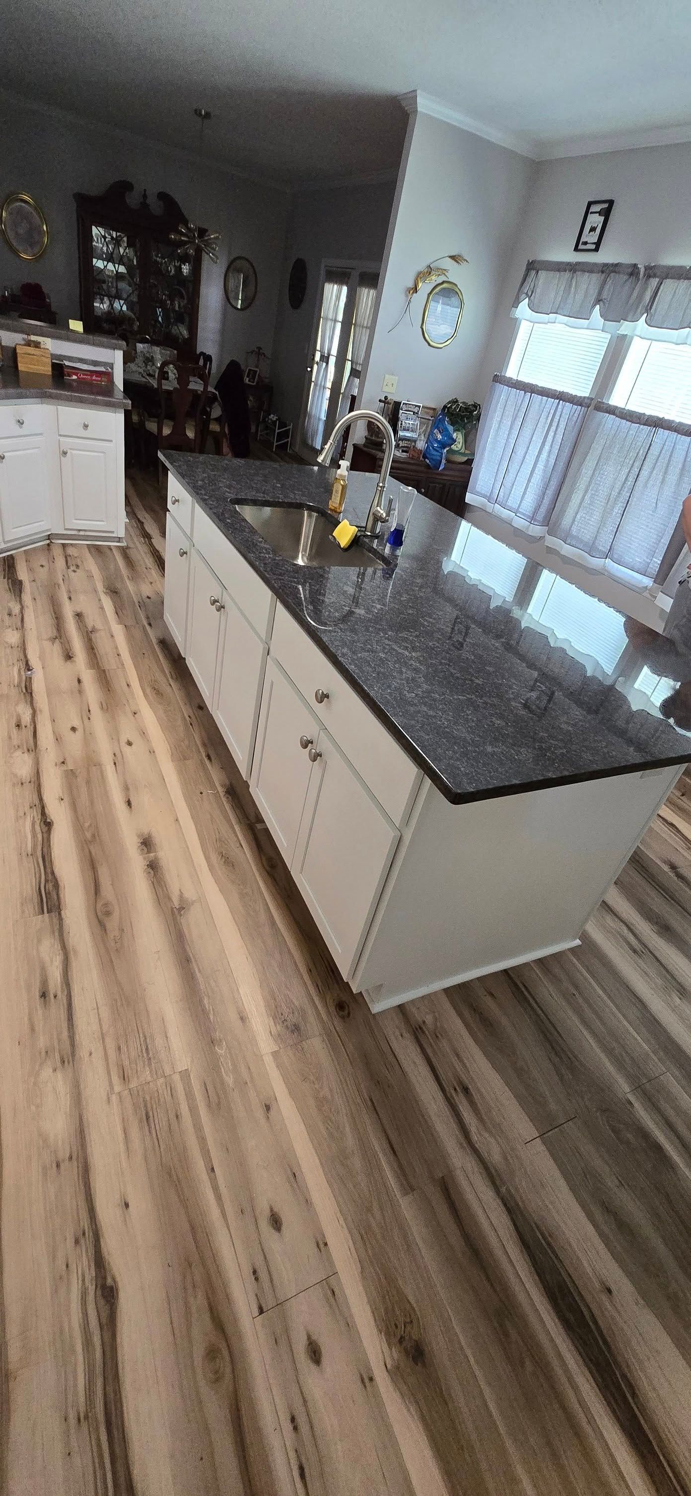 Kitchen with a large island and black granite countertop, white cabinets, and wood-look flooring.