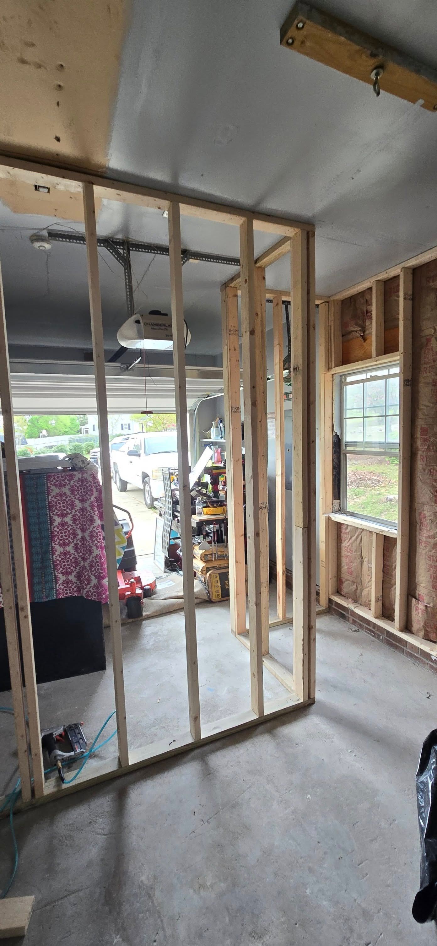 Wooden frame construction inside a garage. A window is on the right, and the garage door is open in the background.