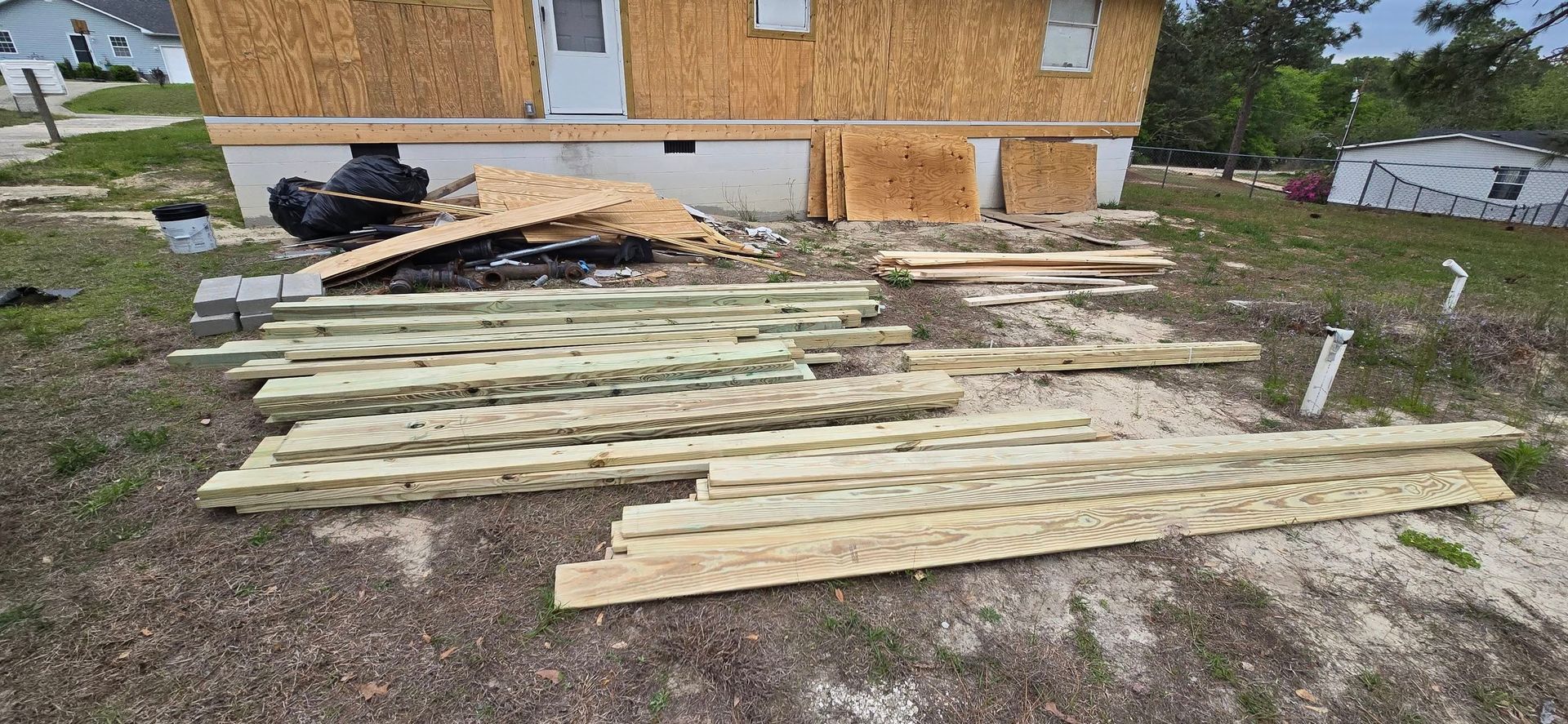 Construction materials on the ground in front of a building with wooden siding, near a residential area.