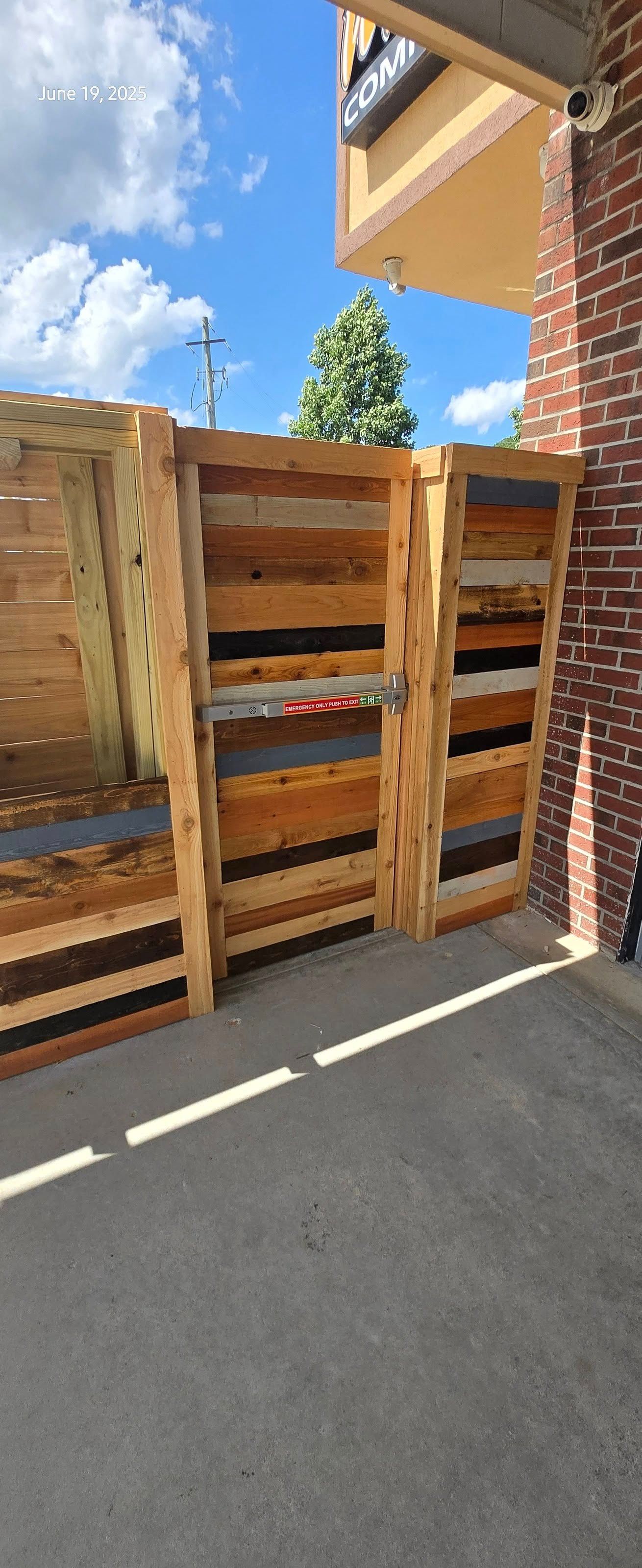 Wooden fence made from reclaimed pallets, next to a brick building.