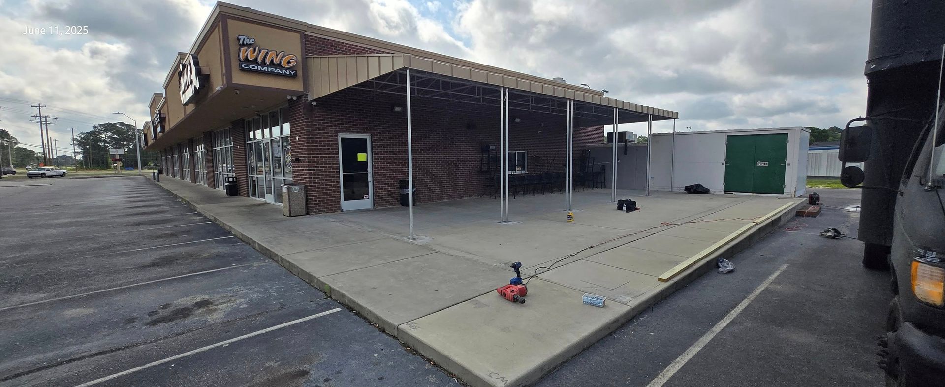Exterior view of a commercial building with a covered patio and a parking lot. Cloudy sky.