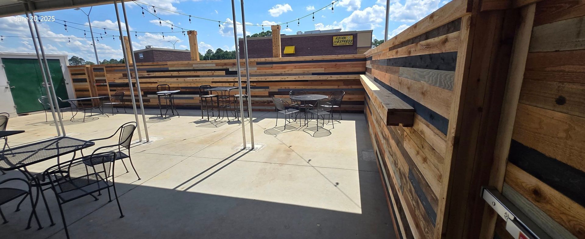 Outdoor patio with wooden fencing, metal tables and chairs, under a blue sky.