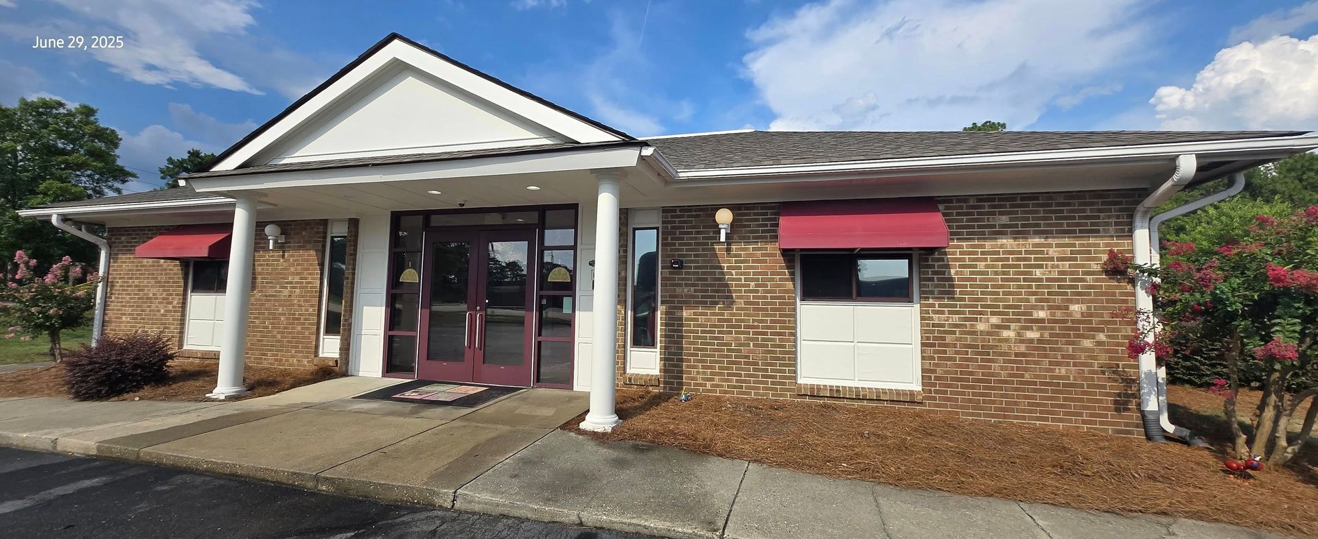 A one-story brick building with a maroon awning and door under a blue sky.