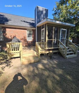 Backyard with a deck and screened porch attached to a brick house. Sunny day with shadows.