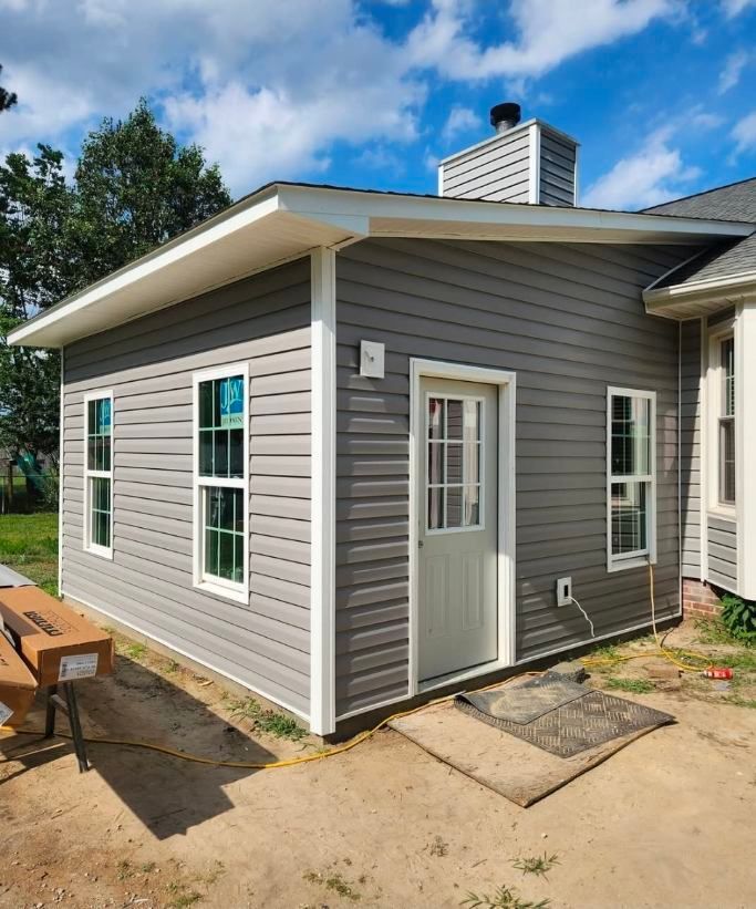 Gray-sided addition with white trim and door. Windows on sides. Chimney visible. Exterior construction site.