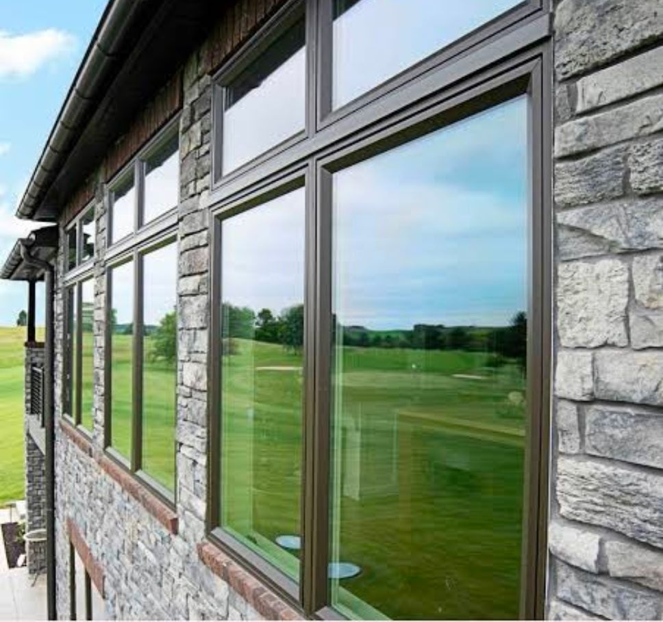 Stone house exterior with a row of large windows reflecting a green golf course and blue sky.