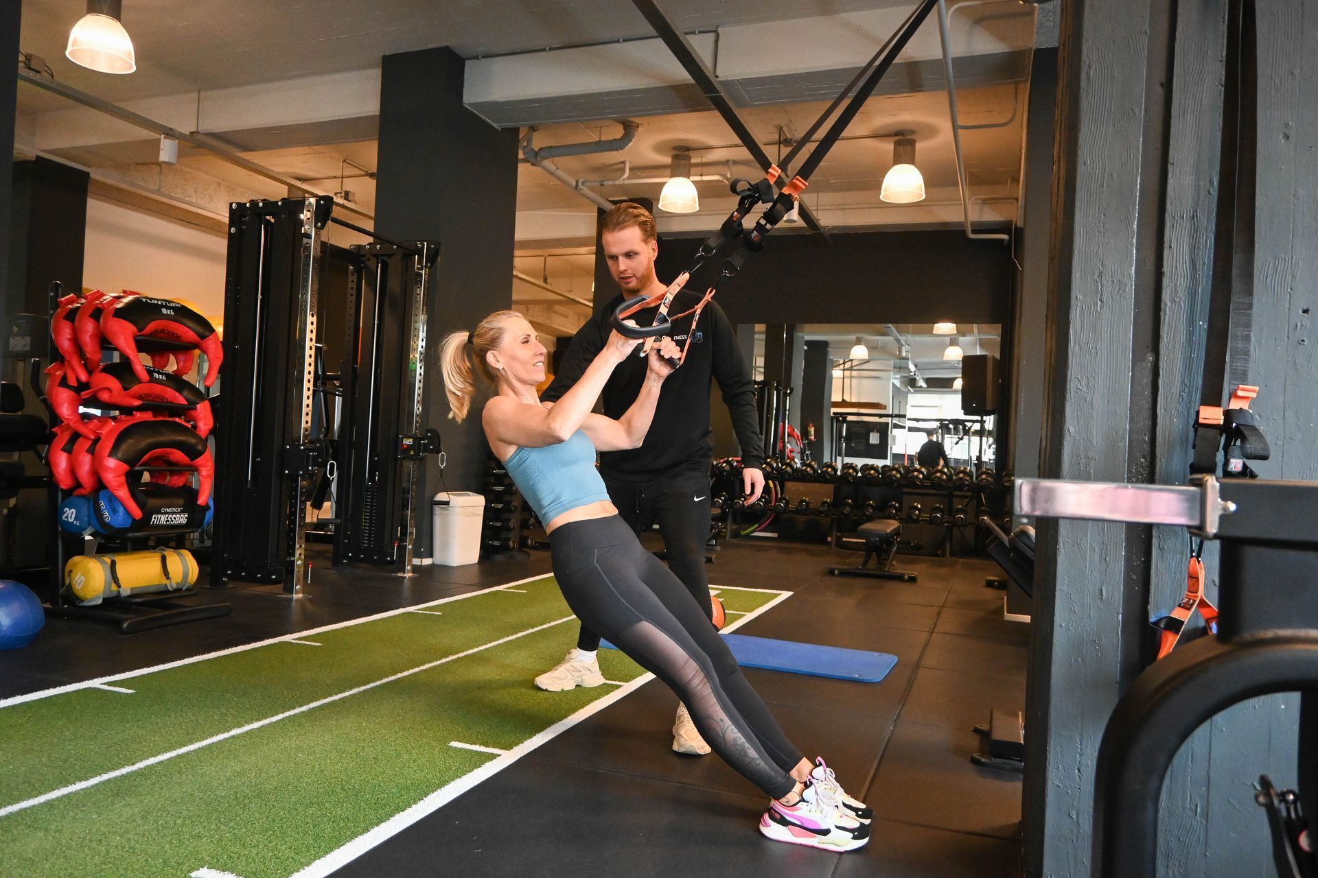 Een man helpt een vrouw met het gebruiken van een apparaat in een sportschool.