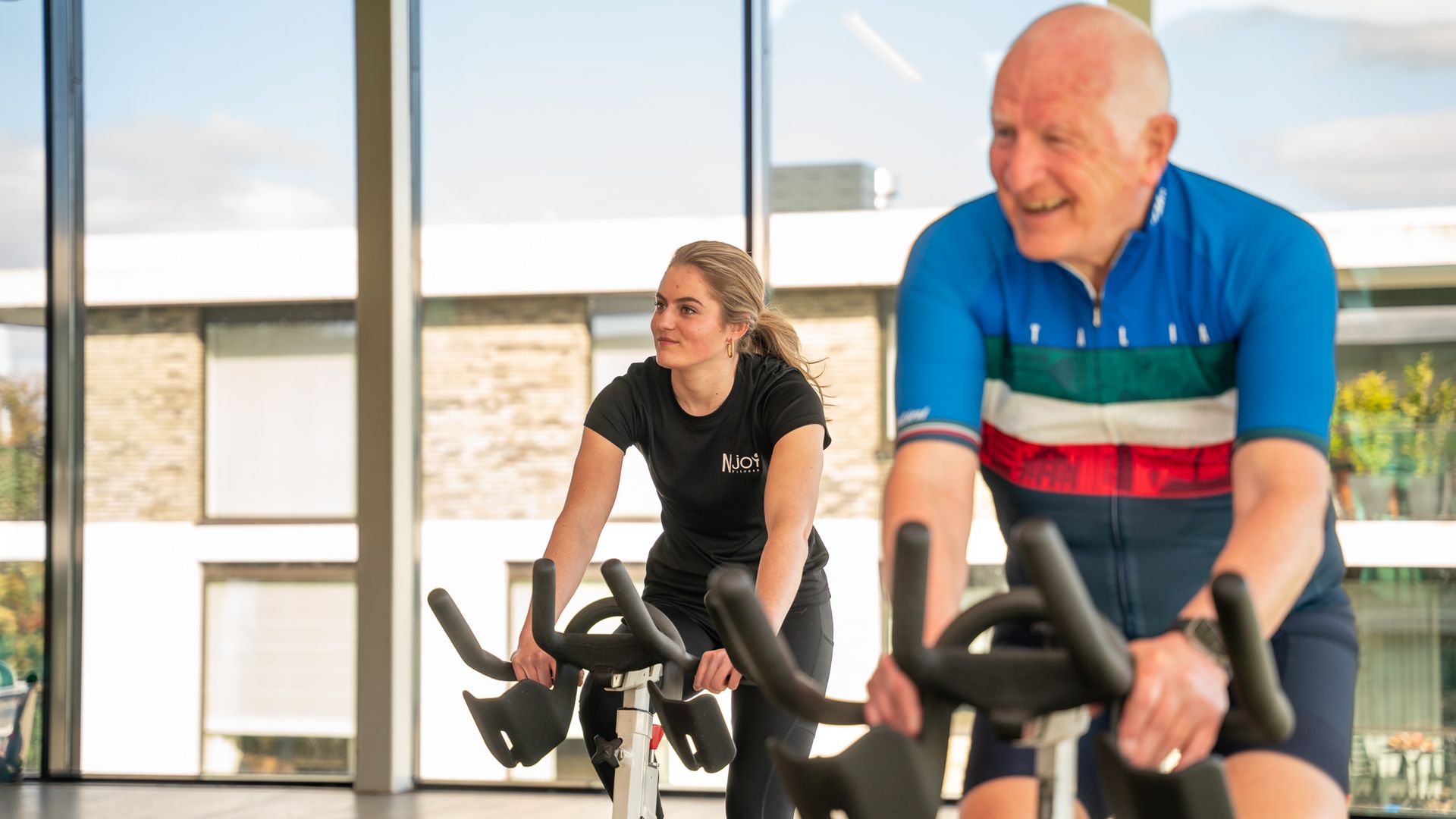 Een man en een vrouw fietsen op een hometrainer in een sportschool.