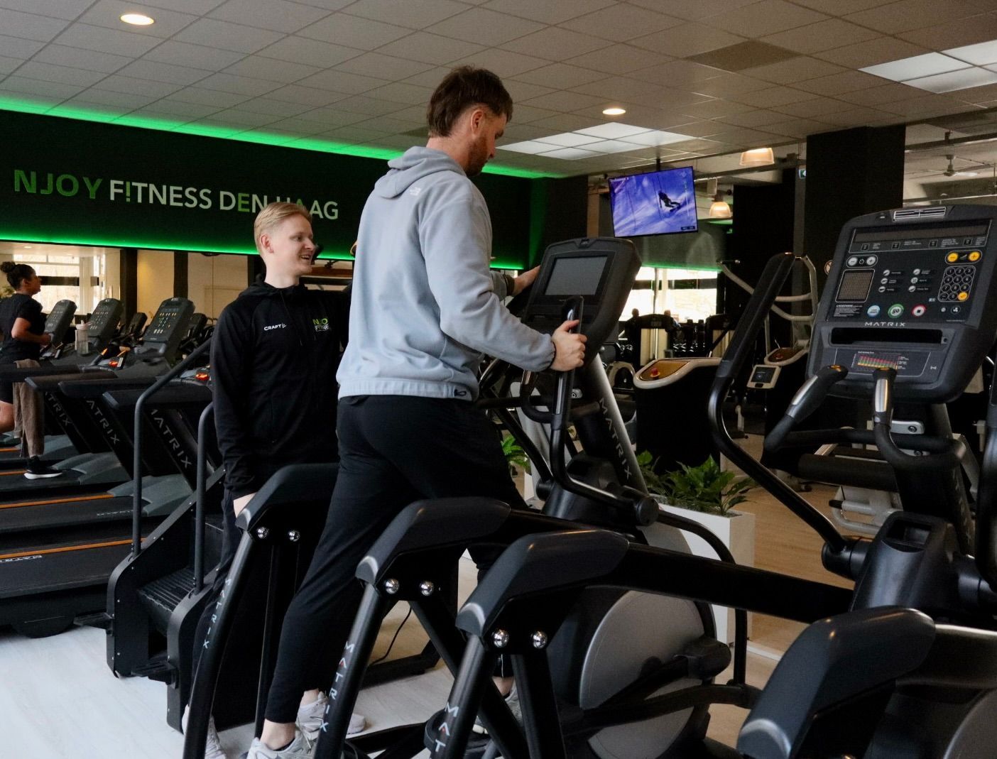 Een man en een vrouw fietsen op een hometrainer in een sportschool.
