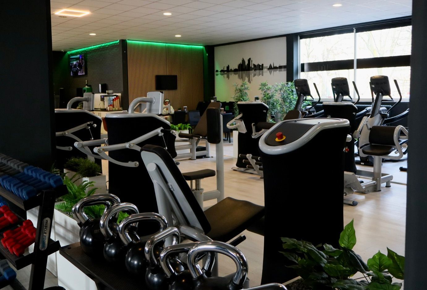 Een sportschool met veel fitnessapparatuur en groene verlichting.
