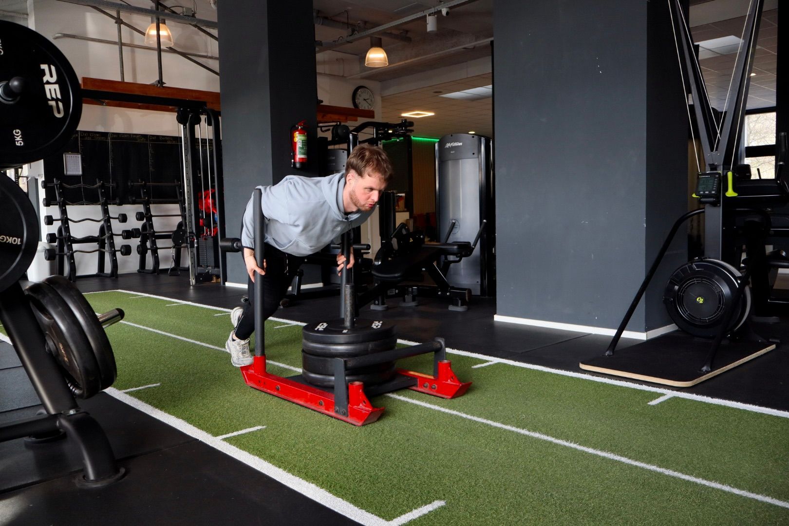 Een man helpt een vrouw met hurken met een halter in een sportschool.