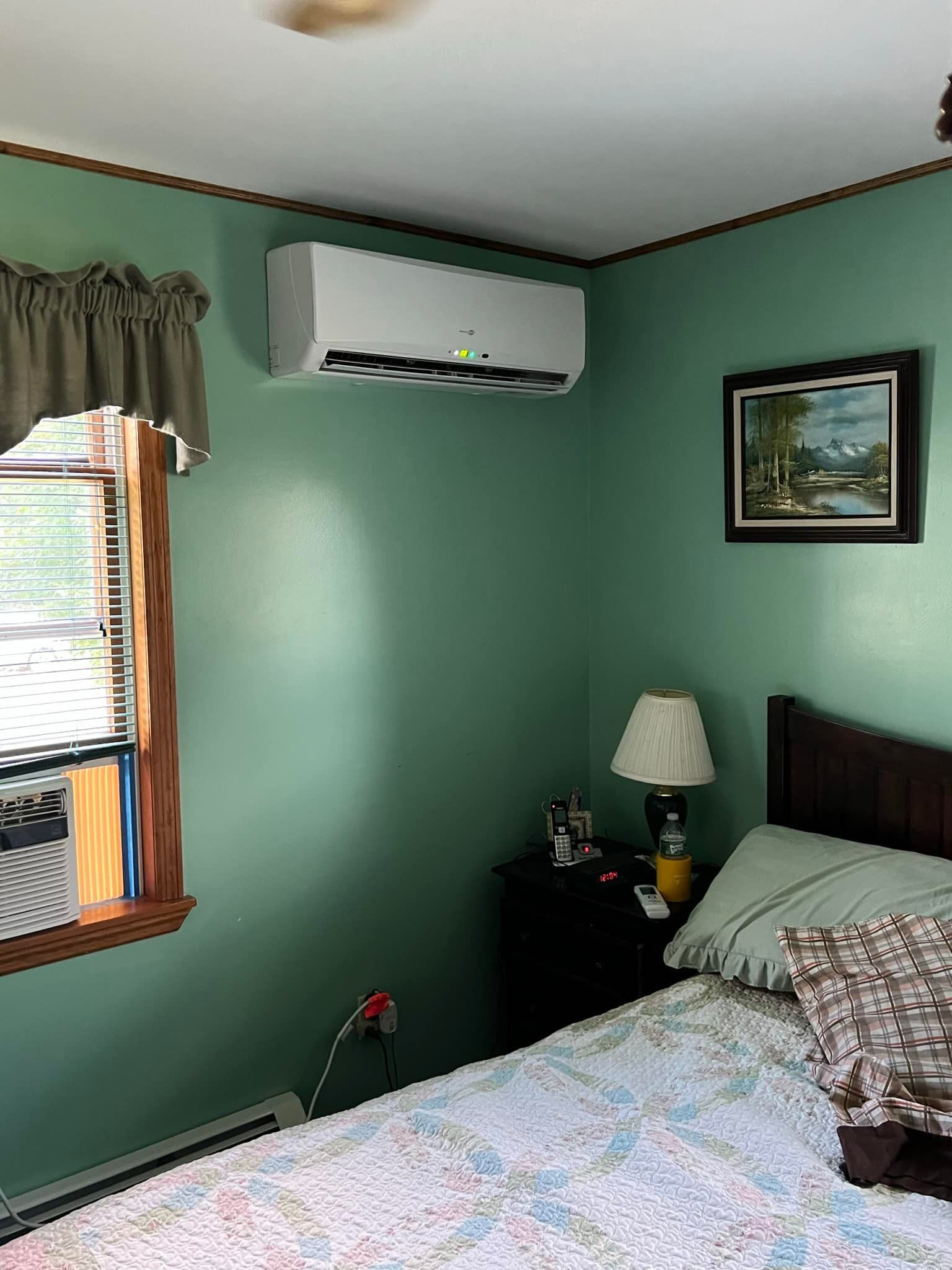 A bedroom with a bed , nightstand , lamp and air conditioner.